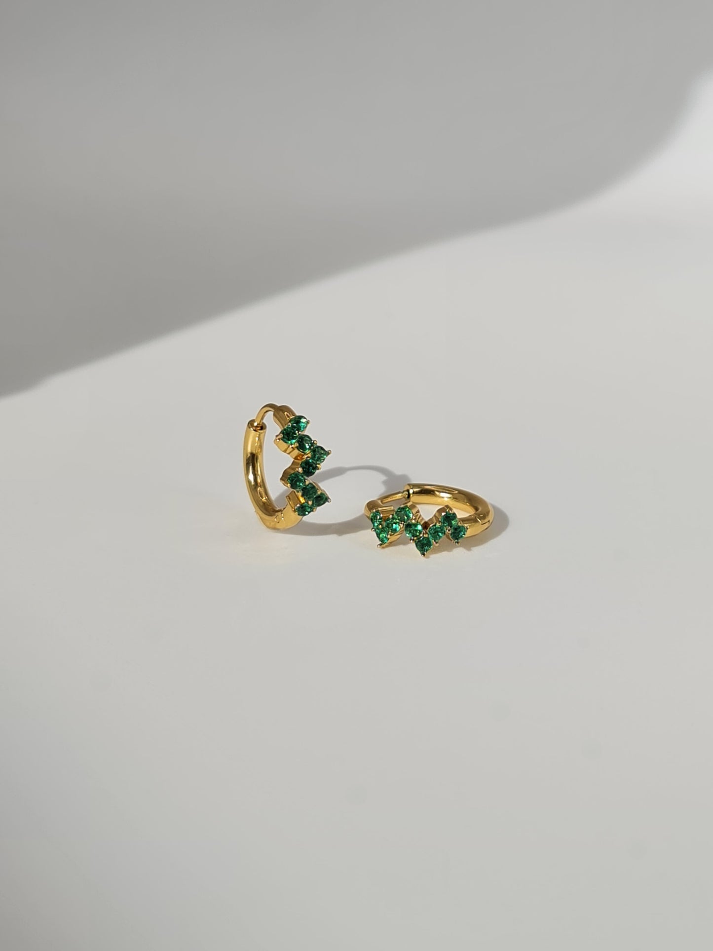 The Lumen 18k Gold Plated Stainless Steel Clustered Crystal Huggie Hoop Earrings in Emerald Green Cubic Zirconia.