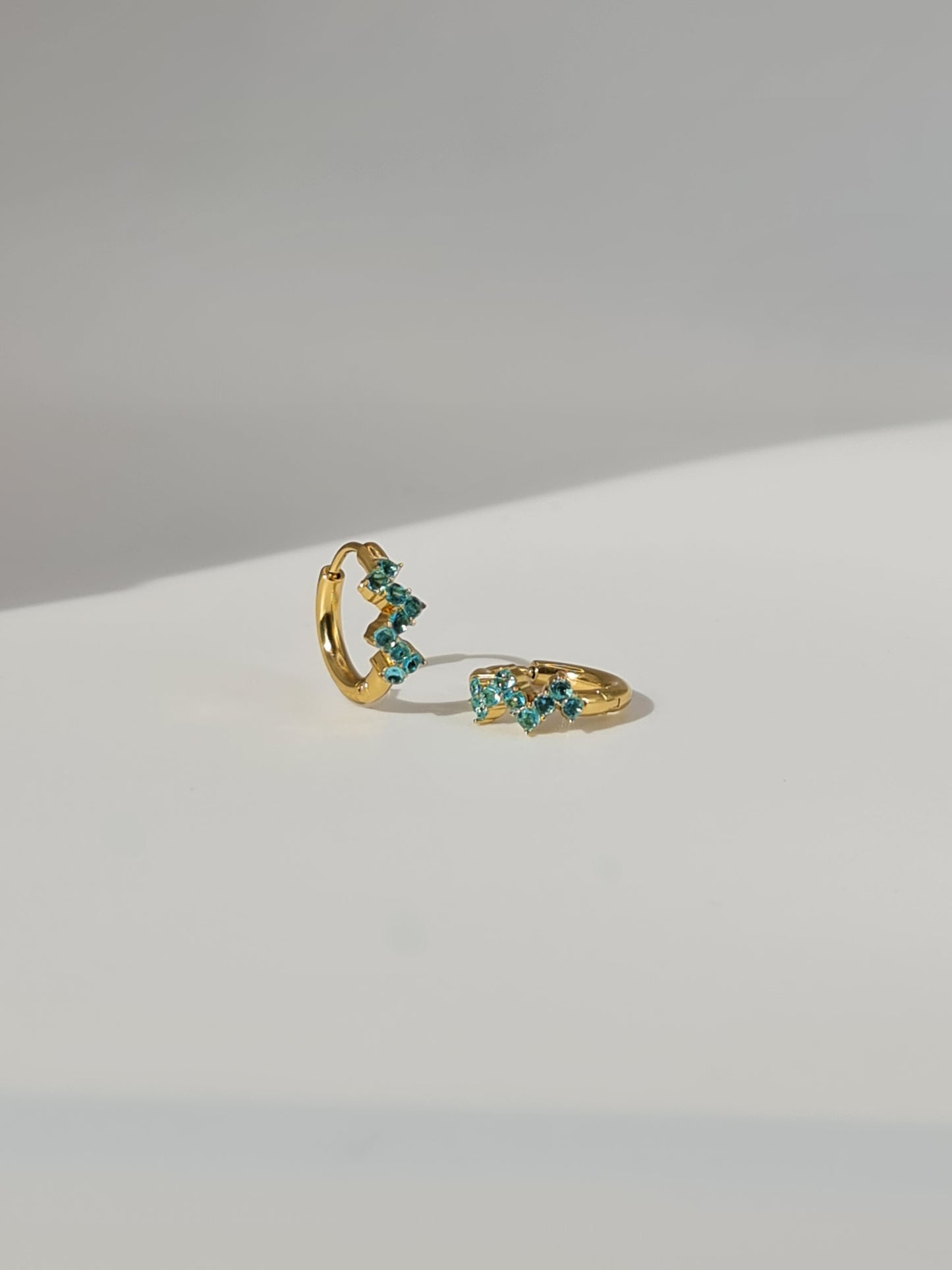 The Lumen 18k Gold Plated Stainless Steel Clustered Crystal Huggie Hoop Earrings in Aquamarine Blue Cubic Zirconia.