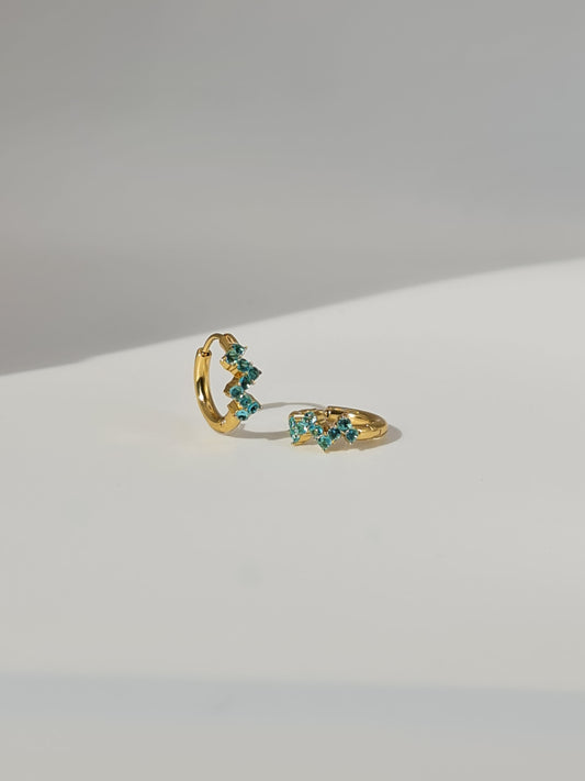 The Lumen 18k Gold Plated Stainless Steel Clustered Crystal Huggie Hoop Earrings in Aquamarine Blue Cubic Zirconia.
