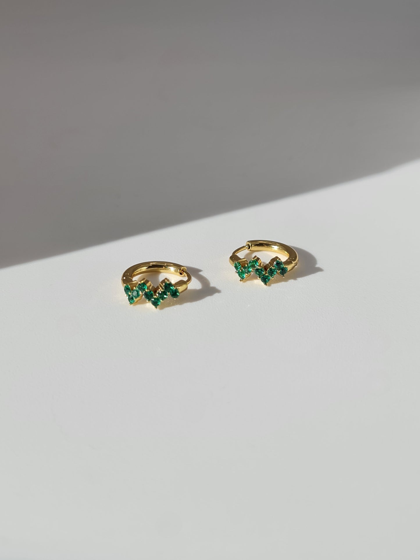 The Lumen 18k Gold Plated Stainless Steel Clustered Crystal Huggie Hoop Earrings in Emerald Green Cubic Zirconia.