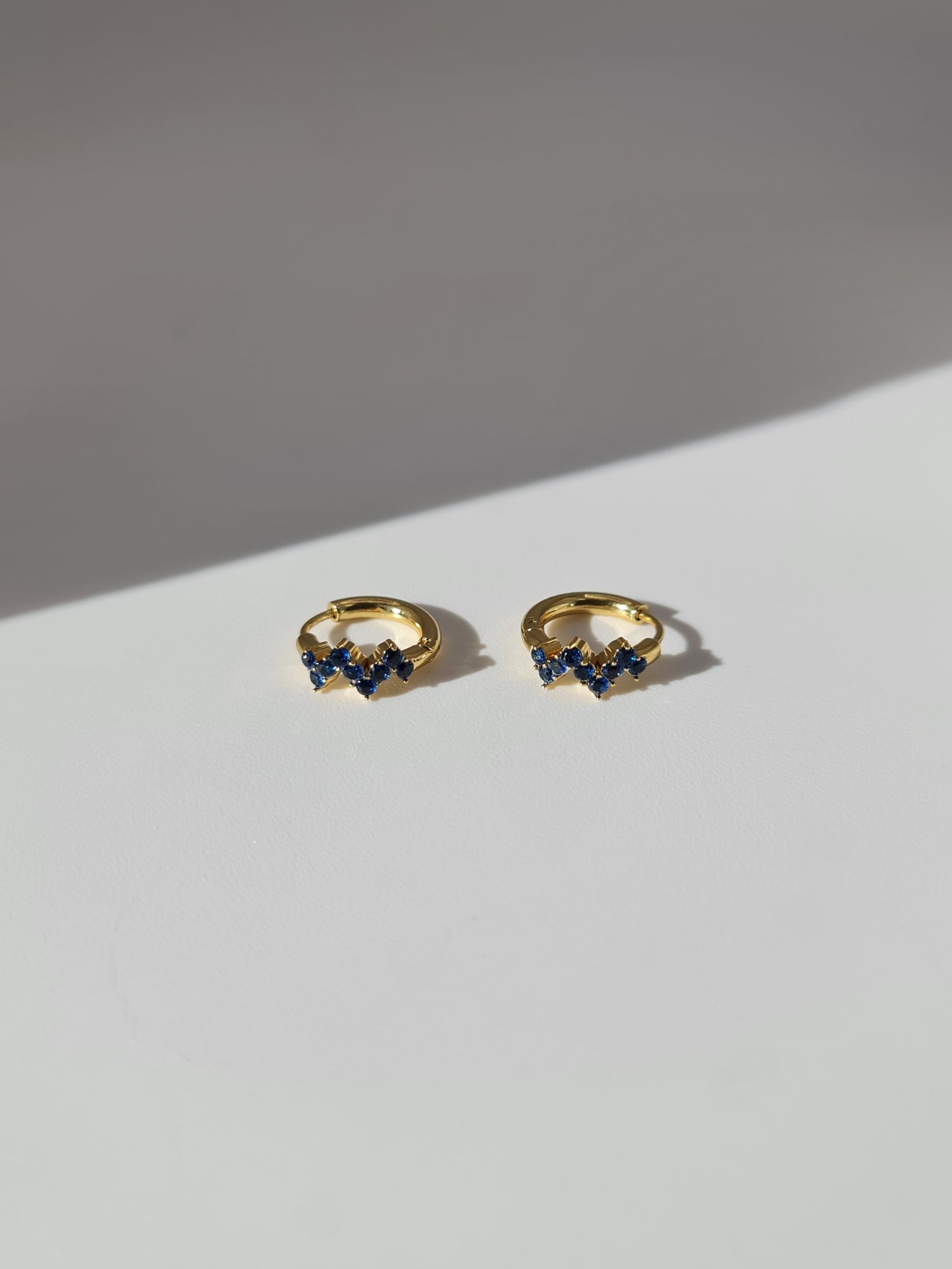 The Lumen 18k Gold Plated Stainless Steel Clustered Crystal Huggie Hoop Earrings in Sapphire Blue Cubic Zirconia.