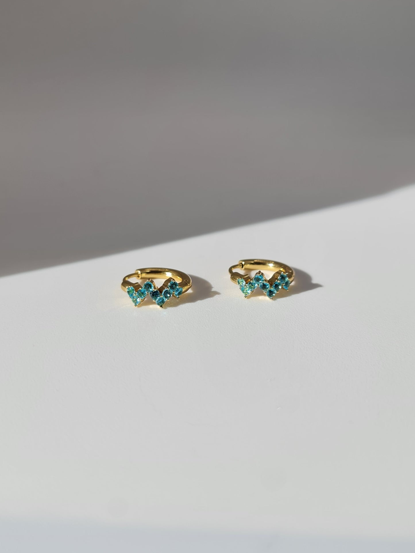 The Lumen 18k Gold Plated Stainless Steel Clustered Crystal Huggie Hoop Earrings in Aquamarine Blue Cubic Zirconia.