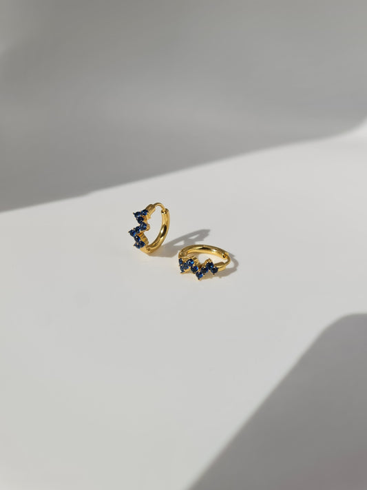 The Lumen 18k Gold Plated Stainless Steel Clustered Crystal Huggie Hoop Earrings in Sapphire Blue Cubic Zirconia.