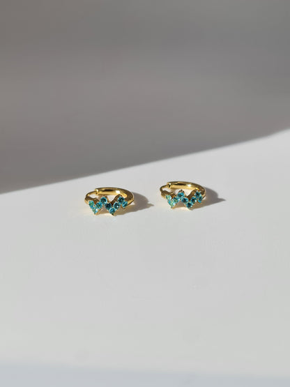 The Lumen 18k Gold Plated Stainless Steel Clustered Crystal Huggie Hoop Earrings in Aquamarine Blue Cubic Zirconia.